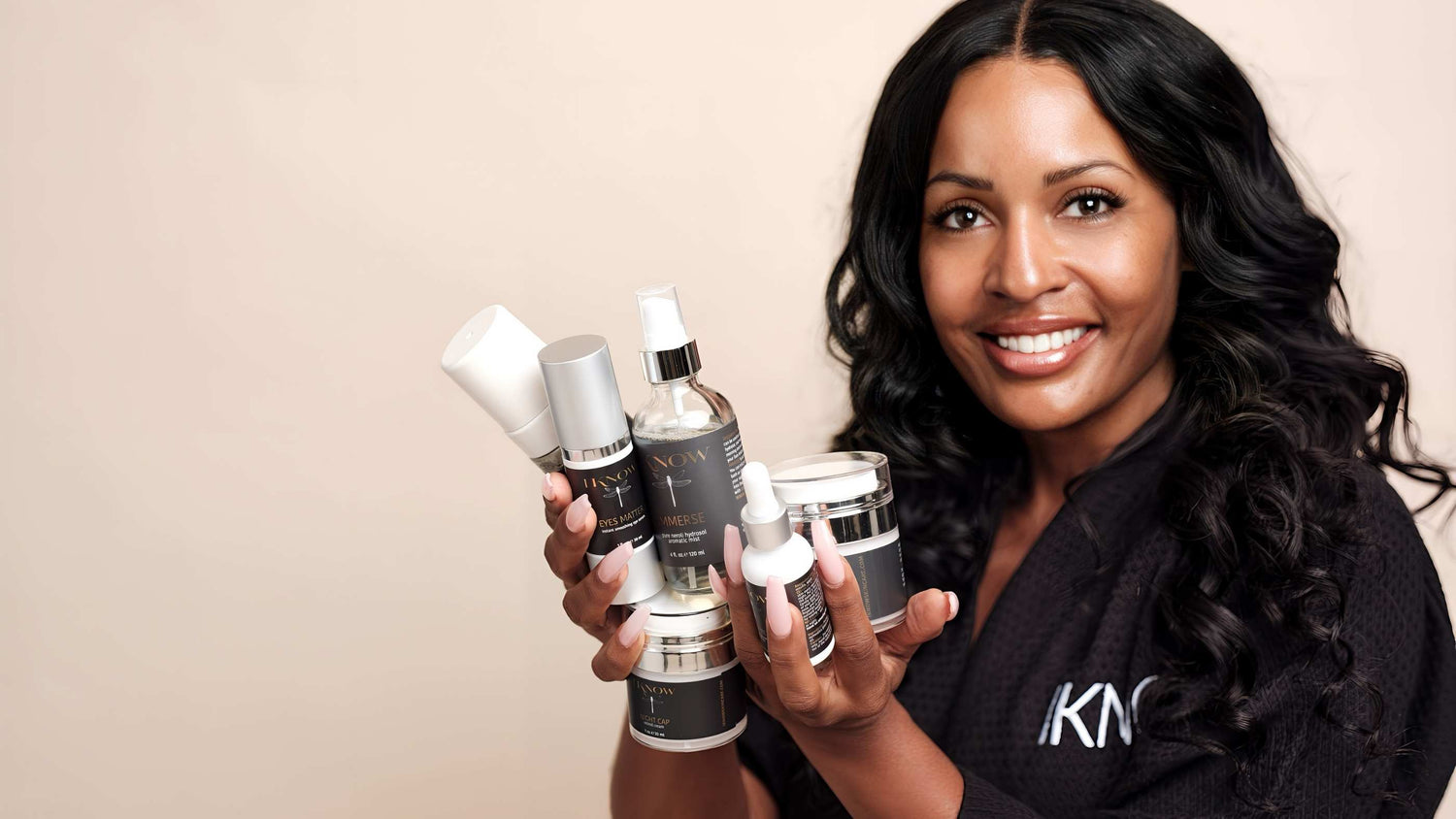 African American woman holding a collection of IKNOW skincare products
