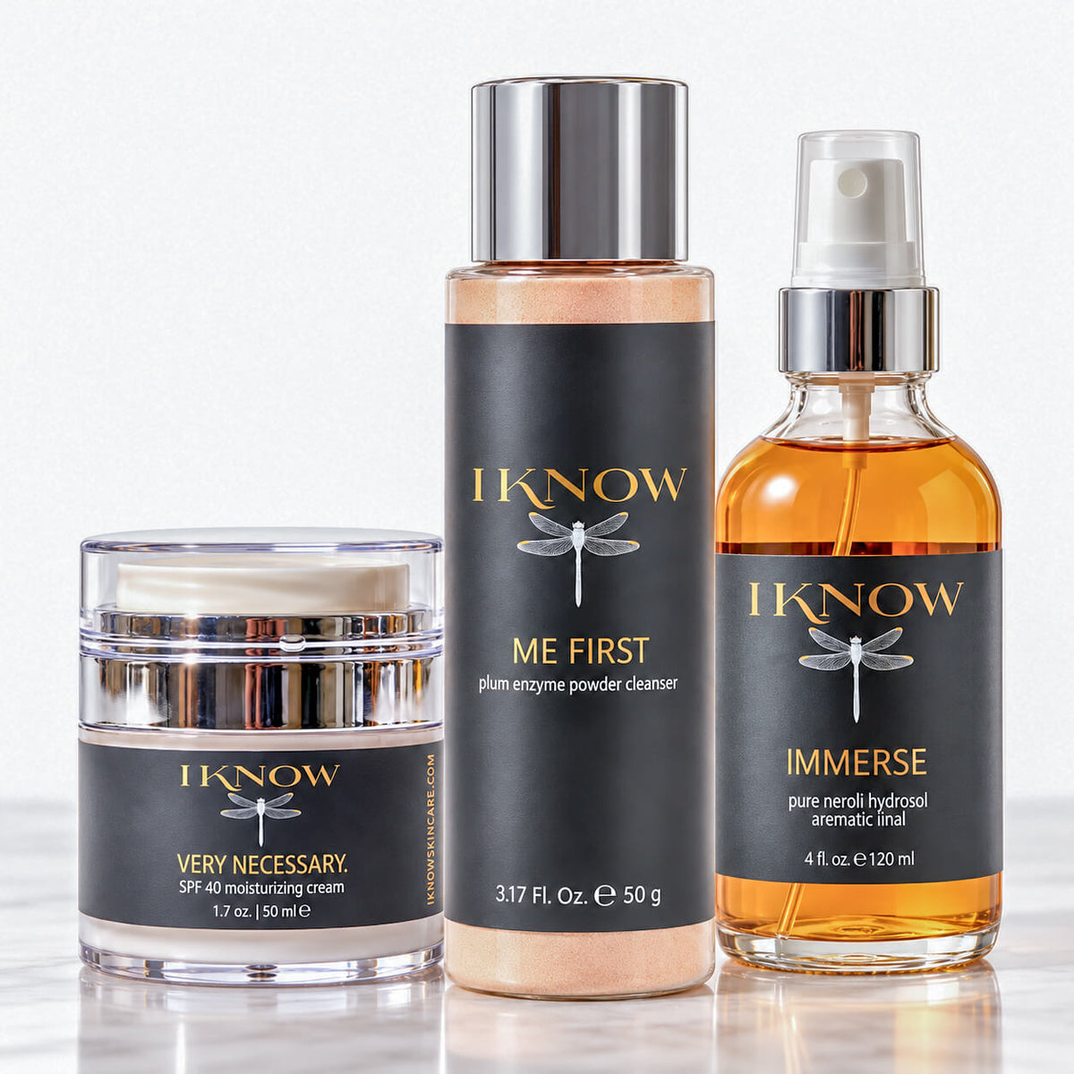 Three skincare products from IKNOW on a clean white background: a clear jar of Very Necessary SPF 40 moisturizer cream, a bottle of Plum Enzyme Powder Cleanser, and a bottle of Immerse pure neroli hydrosol aromatic mist.
