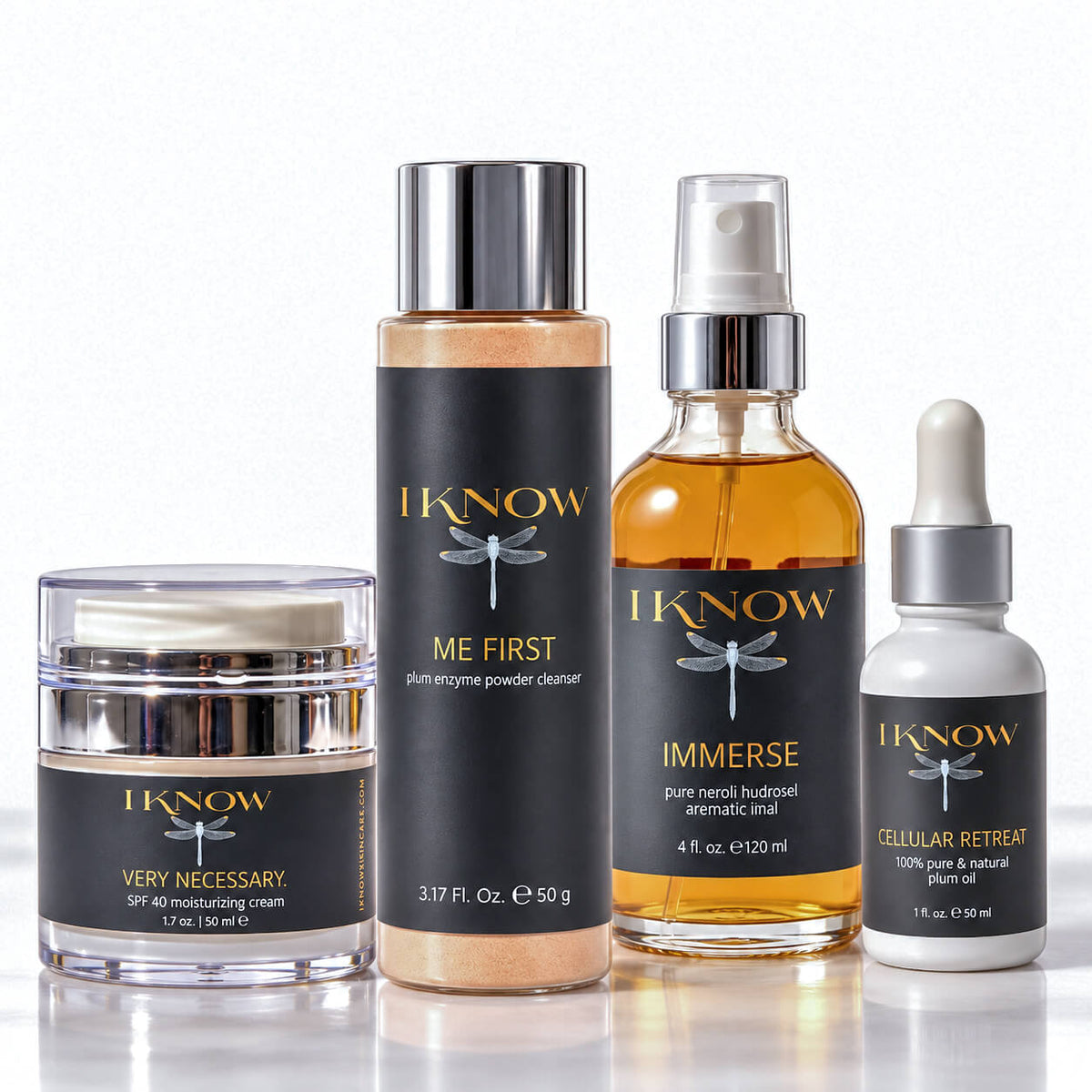 Four skincare products from IKnow Cosmetics arranged on a reflective white surface against a white background: a jar of Very Necessary SPF 40 moisturizing cream, a bottle of Me First exfoliating powder cleanser, a bottle of Immerse pure neroli budget aromatic inhaler, and a dropper bottle of Cellular Retain 100% pure &amp; natural plant serum.