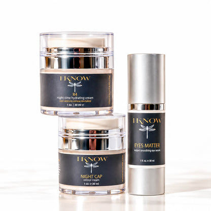 Three skincare products from I Know Beauty arranged on a white reflective surface: a stacked pair of clear jars with black labels and silver lids, and one tall silver cylindrical bottle labeled Eyes Matter.